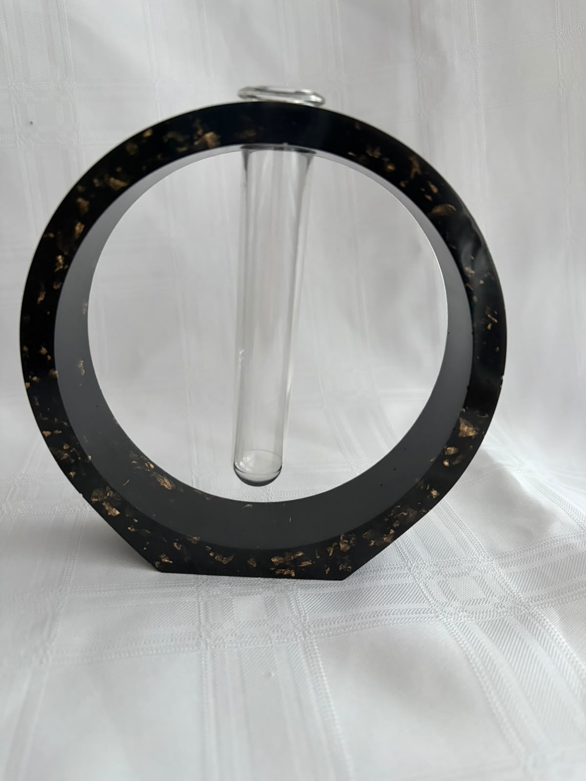 Circular black resin vase with gold leaf suspended in it, holding a glass test tube